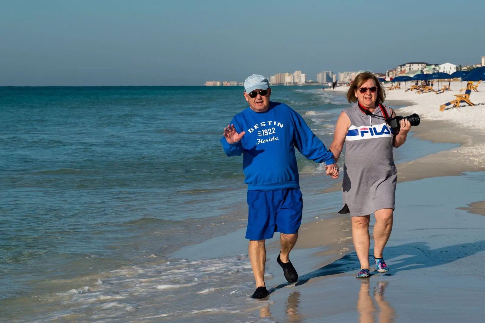 A smiling couple in their sixties walking hand in hand on the beach in Destin, Florida